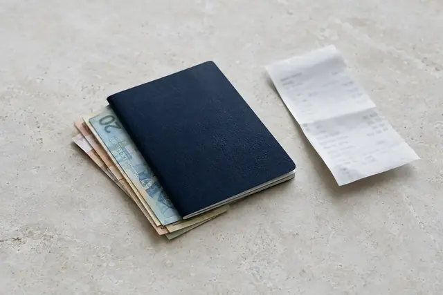 Açık renk zeminde pasaportun altında duran banknotlar ve katlanmış ödeme makbuzu